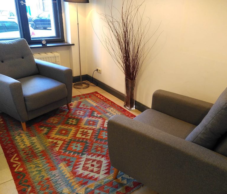 zwei graue gemütliche Sessel stehen sich gegenüber auf einem bunten Teppich und einer Stehlampe in der Ecke als Beleuchtung